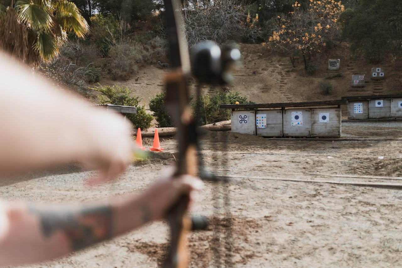 An archer aims at targets at an outdoor archery range, featuring a natural backdrop.