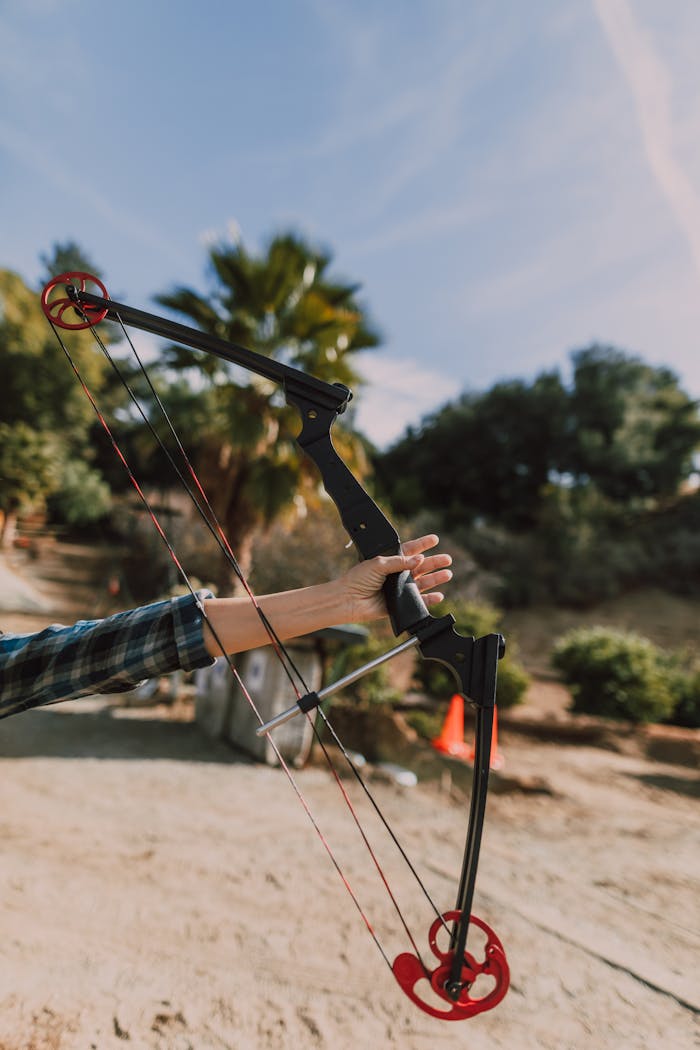 Home A person holding a compound bow outdoors on a sunny day, ready for archery practice.