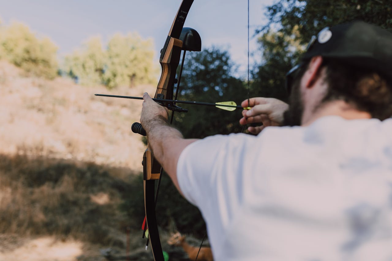A man aiming a recurve bow during archery practice in a natural setting.